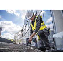 Ein Bauarbeiter kniet und verwendet einen Akku-Bohrschrauber auf einer Baustelle.