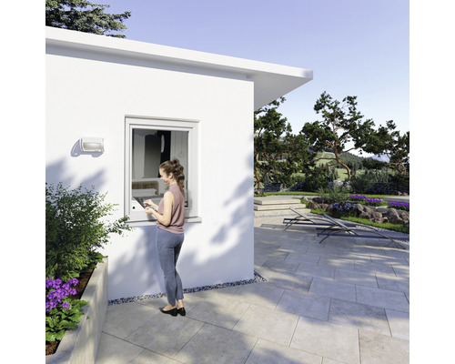 Frau steht vor einem Gartenhaus mit Kunststofffenster und genießt den Blick in den Garten.