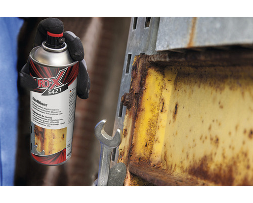 Eine Person mit Handschuhen hält eine Dose Rostlöser neben einem verrosteten Metallstück.