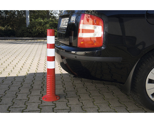 Rot-weißer Warnpfosten neben einem Auto auf einem Parkplatz.