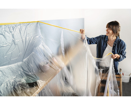 Frau befestigt Abdeckfolie mit Klebeband für Renovierungsarbeiten