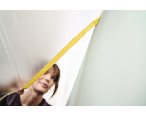 Frau befestigt Abdeckfolie mit Klebeband an der Wand