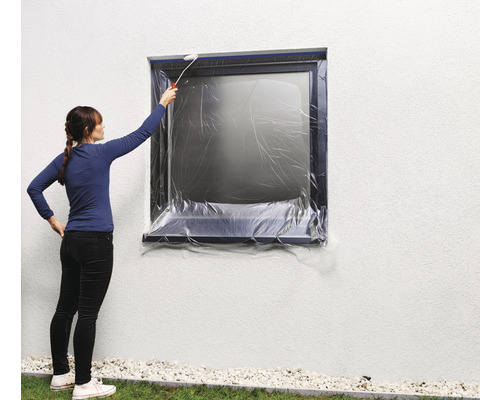 Frau streicht eine Hauswand mit abgedecktem Fenster.