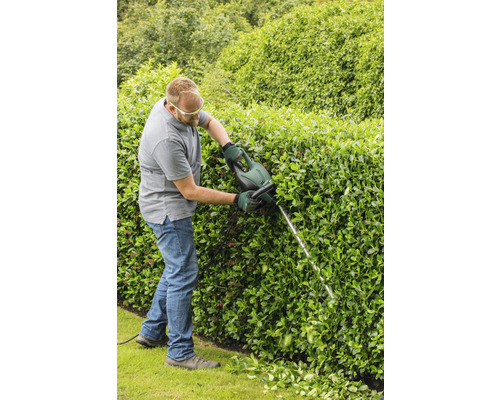 Ein Mann schneidet eine Hecke mit einer Heckenschere.