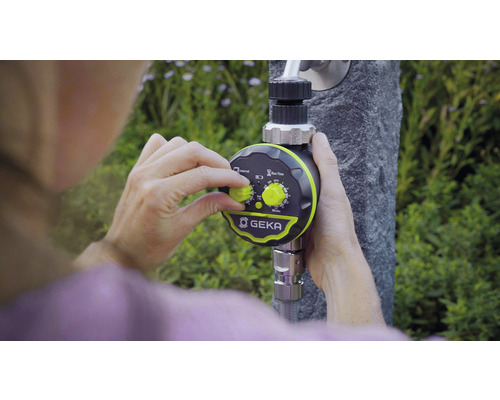 Eine Person stellt die Bewässerungssteuerung von GEKA ein, die an einem Wasserhahn befestigt ist.