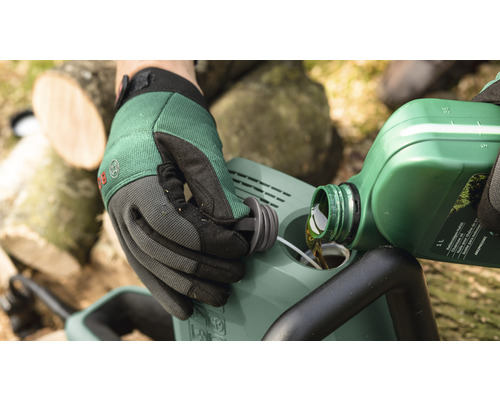 Eine Person füllt Kettenöl in eine Kettensäge. Handschuhe werden getragen.