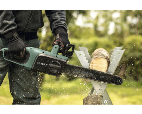 Eine Person sägt mit einer Bosch Elektro Kettensäge ein Stück Holz auf einem Sägebock.