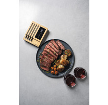 Ein Teller mit geschnittenem Steak, Kartoffeln, Tomaten, zwei Gläsern Wein und einem Fleischthermometer