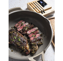Gebratenes Steak in einer Pfanne mit einem Fleischthermometer im Hintergrund