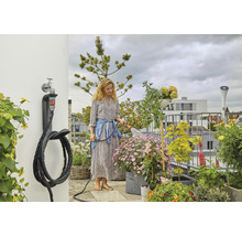 Frau bewässert Pflanzen auf einem begrünten Dachgarten mit einem Gartenschlauch