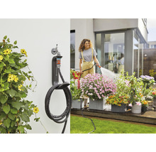 Gartenszene mit Wand-Schlauchbox und Frau, die Blumen gießt