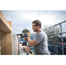 Mann mit Schutzbrille, Gehörschutz und Akku-Schlagschrauber bei der Arbeit an einer Holzkonstruktion