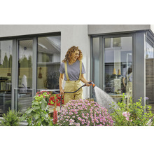 Frau gießt Blumen mit einem Gartenschlauch im Garten.