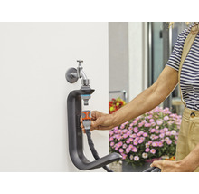 Gartenszene mit Wasserhahn, Schlauchverbinder und Schlauchhalterung zur Bewässerung