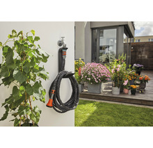 Gartenszene mit Pflanzen, Terrasse und aufgerolltem Gartenschlauch mit Wandhalterung