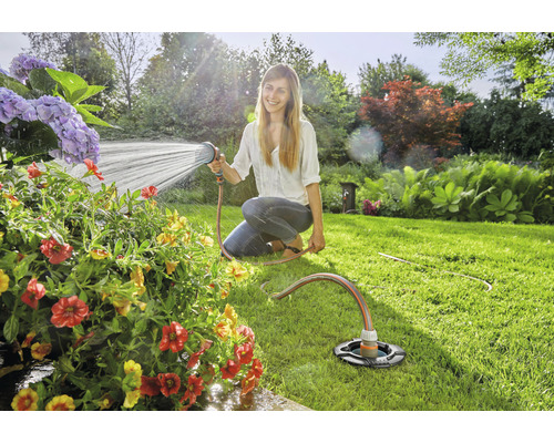 Frau bewässert Blumen mit einem Gartenschlauch und einem Rasensprenger im Garten.