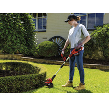 Frau benutzt einen Akku-Rasentrimmer im Garten.