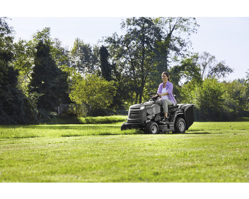 Eine Frau fährt einen Rasentraktor auf einer Wiese.