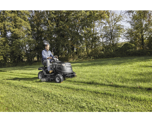 Mann fährt Rasentraktor auf einer Wiese.