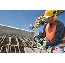 Ein Bauarbeiter mit Schutzhelm und Gehörschutz bearbeitet mit einem Winkelschleifer Stahlträger auf einer Baustelle