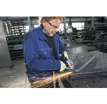 Ein Mann schleift Metall mit einem Winkelschleifer in einer Werkstatt.