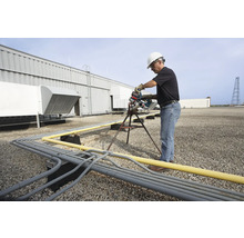 Ein Mann mit Schutzhelm sägt mit einer Rohrsäge ein Rohr auf einem Dach.