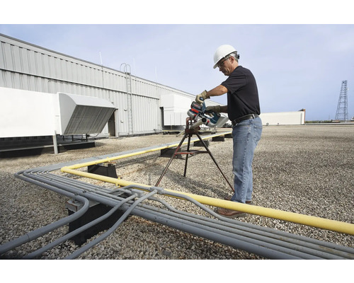 Ein Mann mit Schutzhelm sägt mit einer Rohrsäge ein Rohr auf einem Dach.