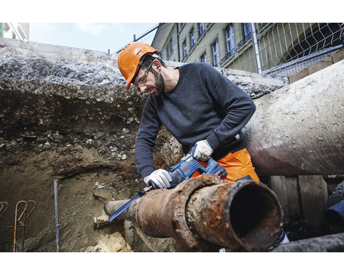Mann mit Schutzbrille und Helm sägt Rohr mit einer Säbelsäge