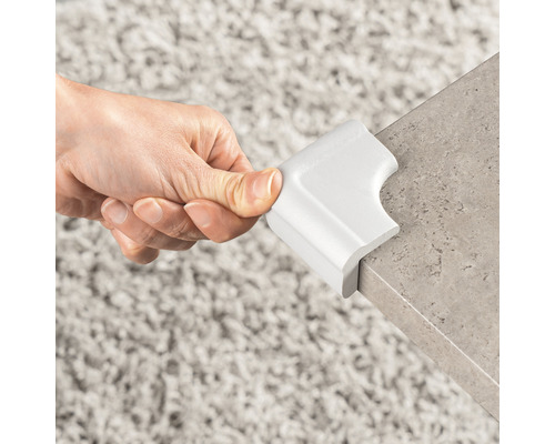 Hand befestigt einen weißen Eckenschutz an einer Tischkante.