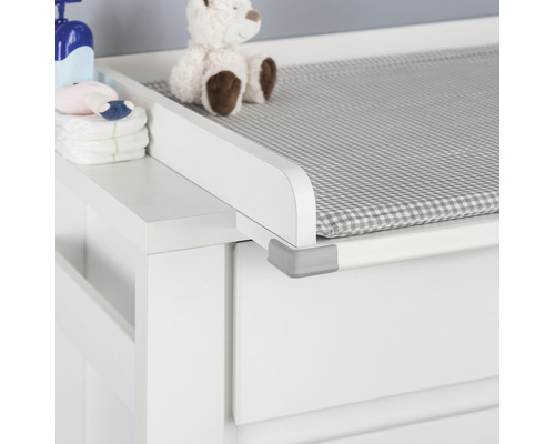 Detailaufnahme eines weißen Wickeltisches mit karierter Auflage, Babypflegeprodukten und einem Teddybär