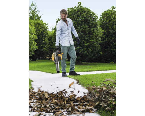 Mann benutzt einen gelben Laubsauger im Garten, um Blätter zu entfernen.