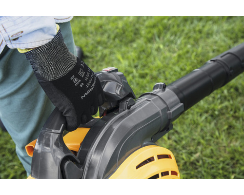 Eine Person bedient einen Laubsauger im Garten und trägt dabei Handschuhe.