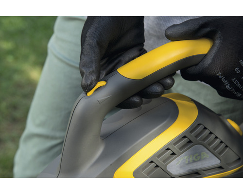 Nahaufnahme einer Person mit Schutzhandschuhen, die einen gelbgrauen Heckenschneider der Marke Stiga bedient.