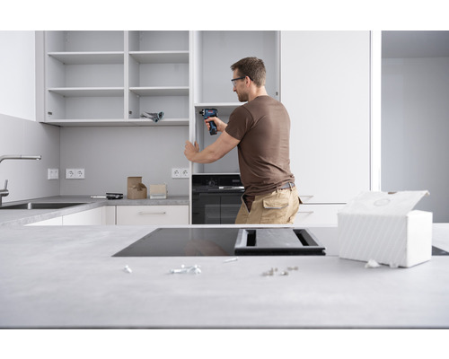 Mann montiert eine Küchenzeile mit einem Akkuschrauber in einer hellen Küche.