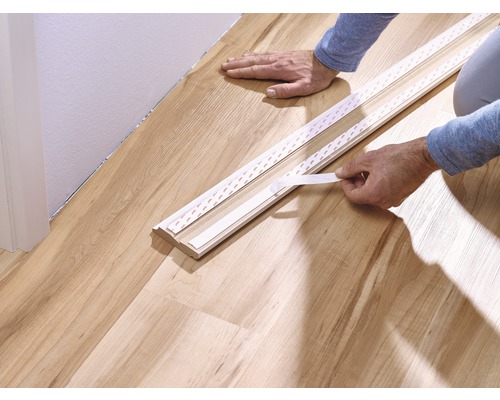Anbringen einer Sockelleiste mit Klebeband auf einem Holzboden.