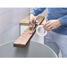Eine Person schneidet doppelseitiges Klebeband mit einer Schere auf einem Holzbrett.
