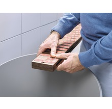 Mann hält Holzbrett mit Klebestreifen über einem Behälter
