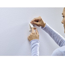 Frau befestigt einen Klebehaken an der Wand