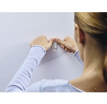 Frau befestigt einen Klebehaken an der Wand