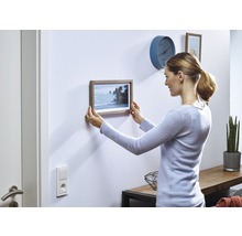 Frau hängt ein Bild mit Holzrahmen an die Wand
