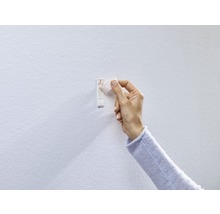 Eine Hand befestigt einen selbstklebenden Bilderhaken an einer Wand.
