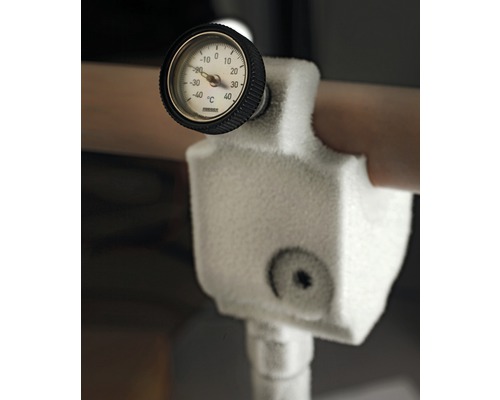 Detailaufnahme eines eingefrorenen Temperaturmessgeräts an einer Rohrleitung