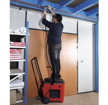 Mann steht auf einem Luftentfeuchter und montiert eine Leitung an der Decke