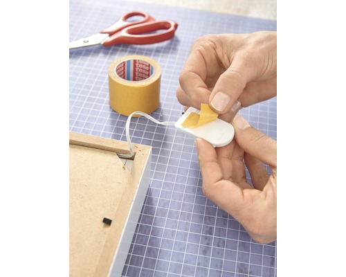 Anbringen einer Lichterkette mit doppelseitigem Klebeband auf der Rückseite eines Bilderrahmens