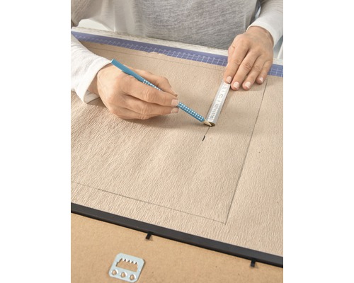 Eine Person zeichnet mit Bleistift und Lineal auf eine Leinwand in einem Bilderrahmen.