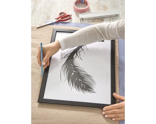 Person rahmt ein Bild mit Federmotiv