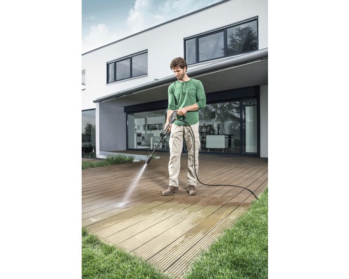 Mann reinigt Holzterrasse mit Hochdruckreiniger vor einem Haus.