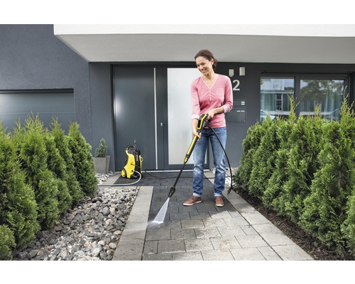 Frau benutzt Hochdruckreiniger zur Reinigung eines Gehweges vor dem Haus