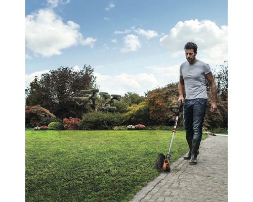 Ein Mann verwendet einen Rasentrimmer auf einem gepflegten Rasen.