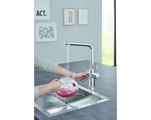 Eine Person befüllt einen Glaskrug mit Wasser an einem Spültisch mit Einhebelmischer.